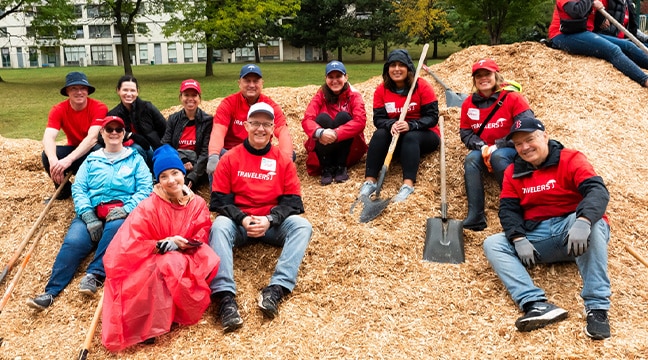 group photo, people sitting on a pile of wood chips with shovels